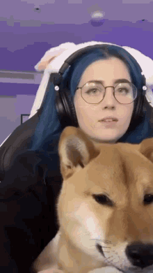 a woman with blue hair and glasses is sitting in a chair with a dog on her lap .