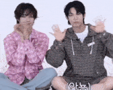 two young men are sitting next to each other on the floor and waving their hands .