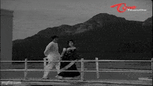 a black and white photo of a man and a woman standing next to each other on a pier .