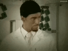 a man in a lab coat and tie is standing in front of a wall with x-rays on it .
