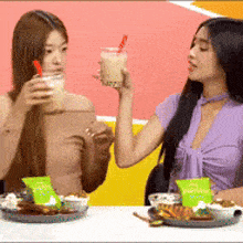 two women are sitting at a table eating food and drinking milkshakes