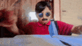 a boy wearing sunglasses and a mustache is sitting at a table