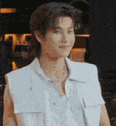 a young man wearing a white vest and a necklace is smiling and making a funny face .