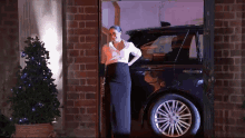 a woman is standing in front of a car with a christmas tree in the background