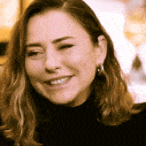 a woman wearing hoop earrings and a black turtleneck is smiling