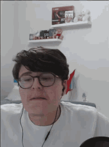 a young man wearing glasses and headphones is sitting in front of a shelf with stuffed animals on it .