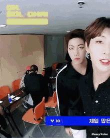 two young men are standing next to each other in a room with a yellow sign that says lol-chan