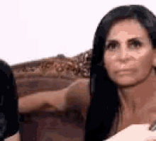 a woman with long dark hair is sitting on a couch looking at the camera .