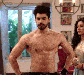 a shirtless man stands in front of a woman in a living room