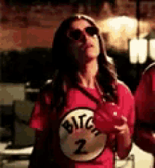 a woman wearing sunglasses and a red shirt with the number 2 on it is holding a glass of wine .