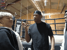 a man in a black shirt with the word pug on it stands in a boxing ring