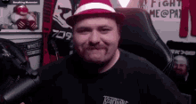 a man wearing a red and white hat is sitting in front of a microphone and smiling .