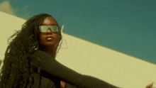 a woman wearing sunglasses and a black dress is dancing in front of a white wall .