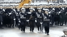 a group of soldiers marching in a parade with a yellow flag in the background .