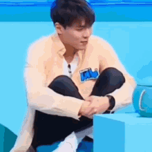 a man is sitting on a blue couch with his legs crossed and his hands on his knees .