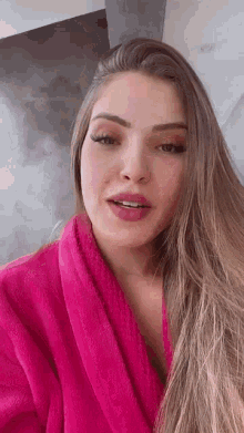 a woman with long hair is wearing a pink robe and talking to the camera .