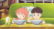 a boy and a girl are sitting on a green couch eating bowls of food with chopsticks