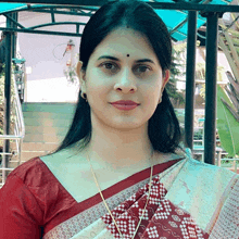 a woman wearing a red and white blouse and a gold necklace smiles for the camera