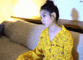 a woman is sitting on a couch wearing a yellow shirt with letters on it