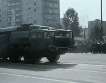 a military vehicle is driving down a street with a crowd behind it