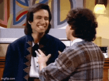 two men are standing next to each other and smiling . one of the men is wearing a blue jacket .