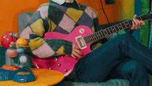 a person in a colorful sweater is playing a pink electric guitar