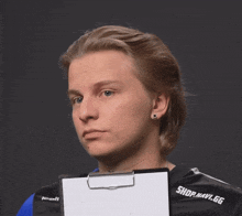 a man wearing a shirt that says shop.navi.gg holds a clipboard in front of his face
