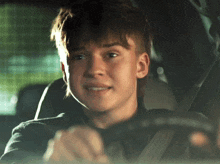 a young boy is driving a car and smiling at the camera