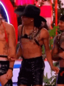 a shirtless man wearing a cowboy hat and leather shorts is standing next to a group of men .