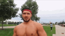 a shirtless man wearing a red headband is walking in a park .