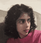 a woman with curly hair wearing a pink shirt looks to the side