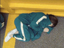a person in a green tracksuit is laying on a yellow carpet .