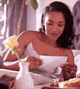 a woman in a white tank top is reading a piece of paper