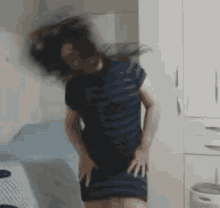 a woman in a blue dress is standing in a room with her hair blowing in the wind .