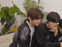 a group of young men are sitting on a couch and one is covering his mouth with his hand .