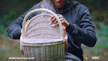 a woman is holding a wicker basket with the nbc logo on the bottom left