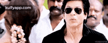 a man wearing sunglasses and a black shirt is standing in a crowd of people .
