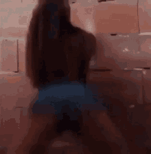 a woman is dancing in front of a brick wall while wearing shorts .