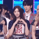 a girl is making a heart shape with her hands while standing in front of a crowd of people .