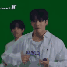 a man in a white shirt is dancing in front of a green screen while another man looks on .