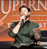 a man in a green shirt is holding a microphone in front of a sign that says supern
