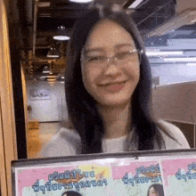 a woman wearing glasses is smiling while holding a sign in a room .