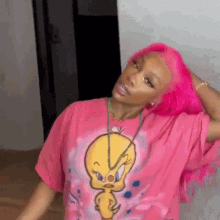 a woman with bright pink hair is wearing a pink t-shirt with tweety on it .