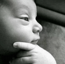a black and white photo of a baby with a hand on his chin .