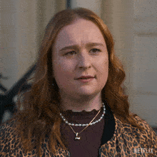 a woman with red hair is wearing a leopard print jacket and a necklace with a p on it