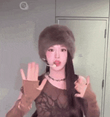 a woman wearing a fur hat and gloves is making a peace sign .