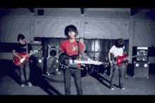 a man in a red shirt is playing a red guitar in a band