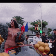 a woman in a crown is standing next to a red car with balloons and a license plate that says 01100