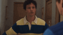 a young man in a yellow and blue striped shirt looks at himself in the mirror
