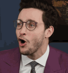 a man wearing glasses and a purple suit has his mouth wide open